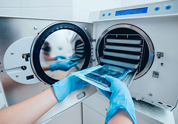 Lab worker with gloves on placing lab tools in autoclave for sterilization