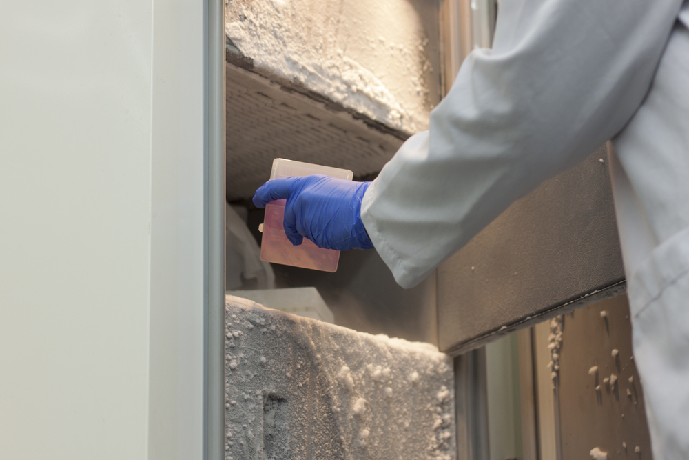 Female scientist with blue gloves on the hand and white uniform putting research samples in ULT freezer