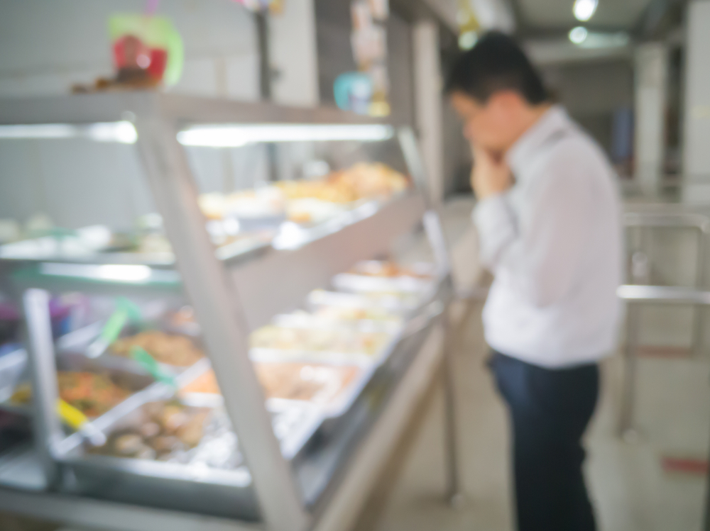 Blurred image of man in hospital cafeteria at food display cabinet and selecting various food
