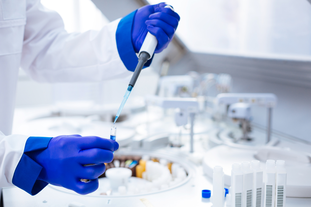 Hands in blue gloves holding pipette and test tube with poured blue chemical which placed on blurred background